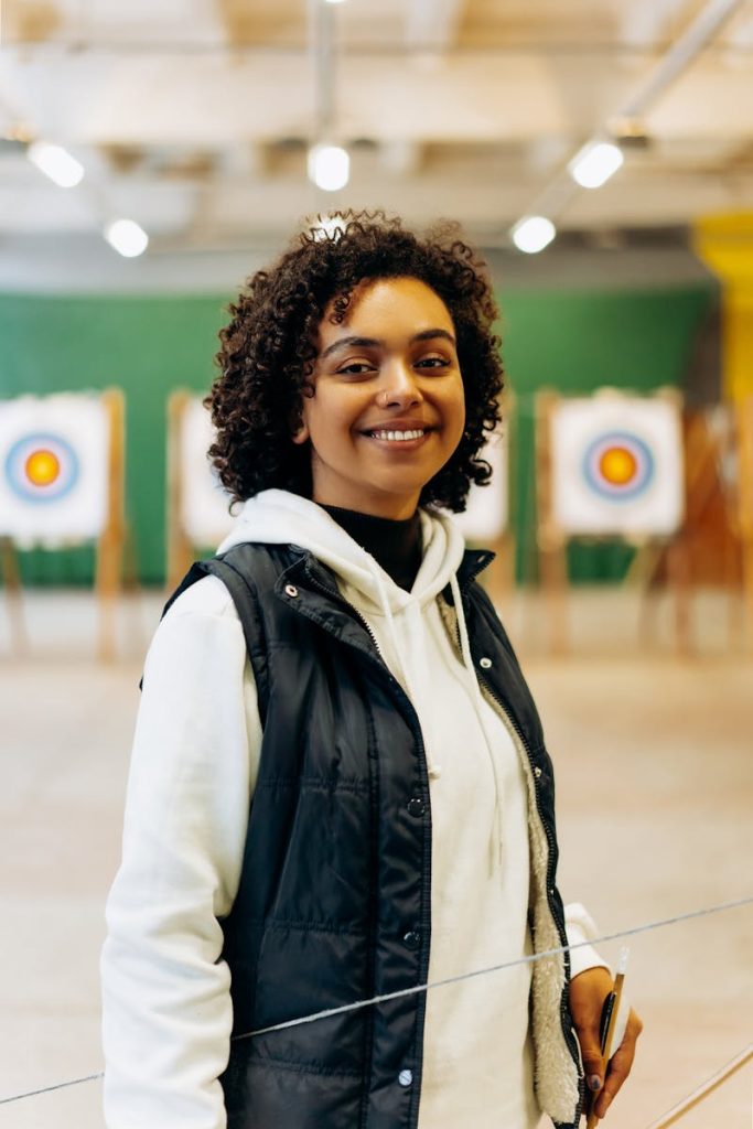 Young woman preparing for archery practice in an indoor range with targets in the background.