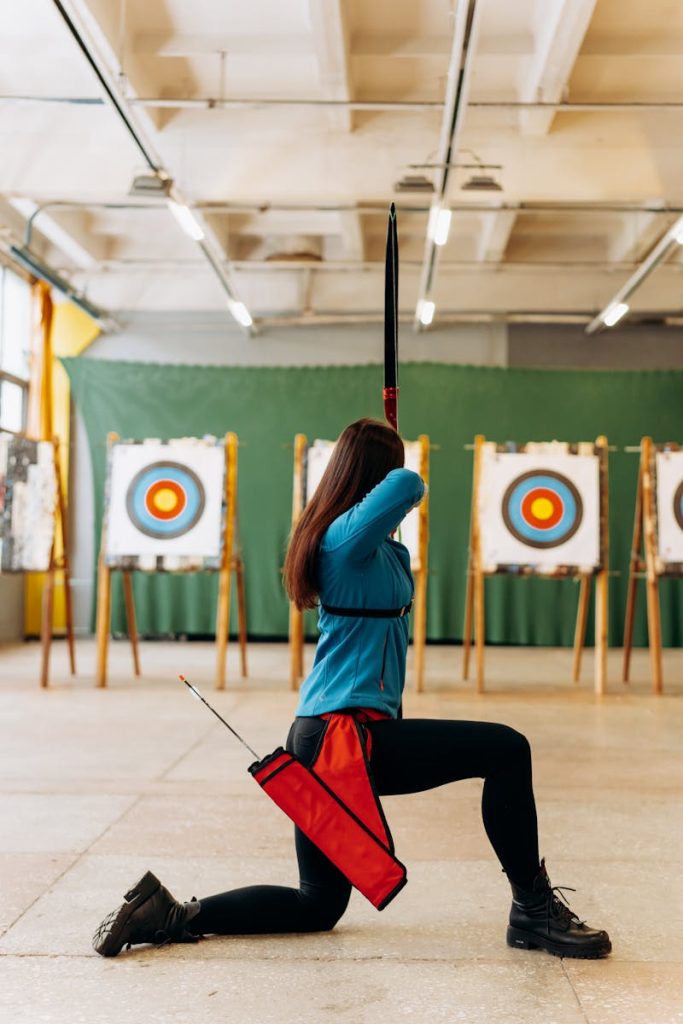 A young woman practicing archery indoors, aiming at a target with focus and precision.